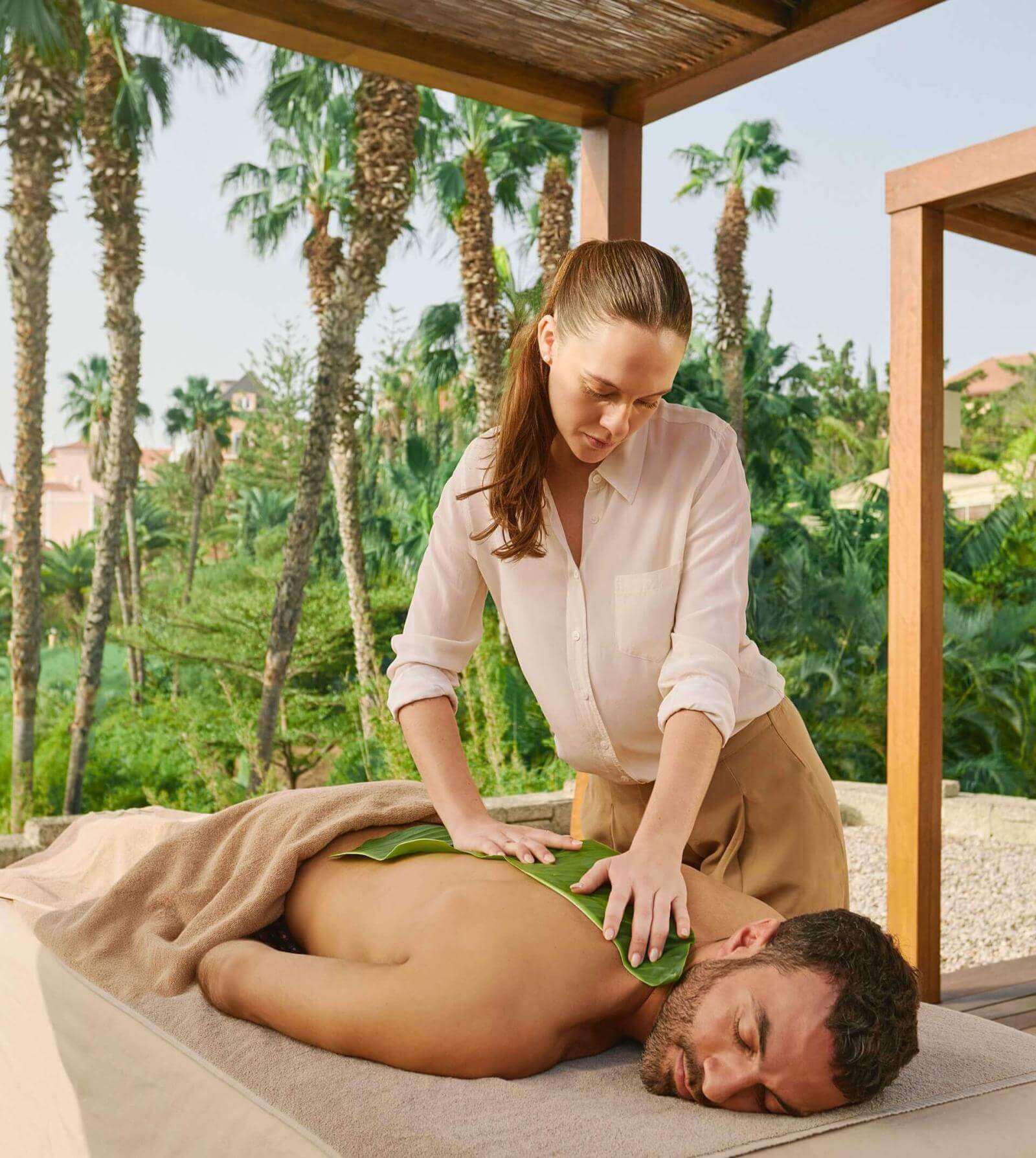 Man geniet van een massage in een hoteltuin met palmbomen onder een pergola. 