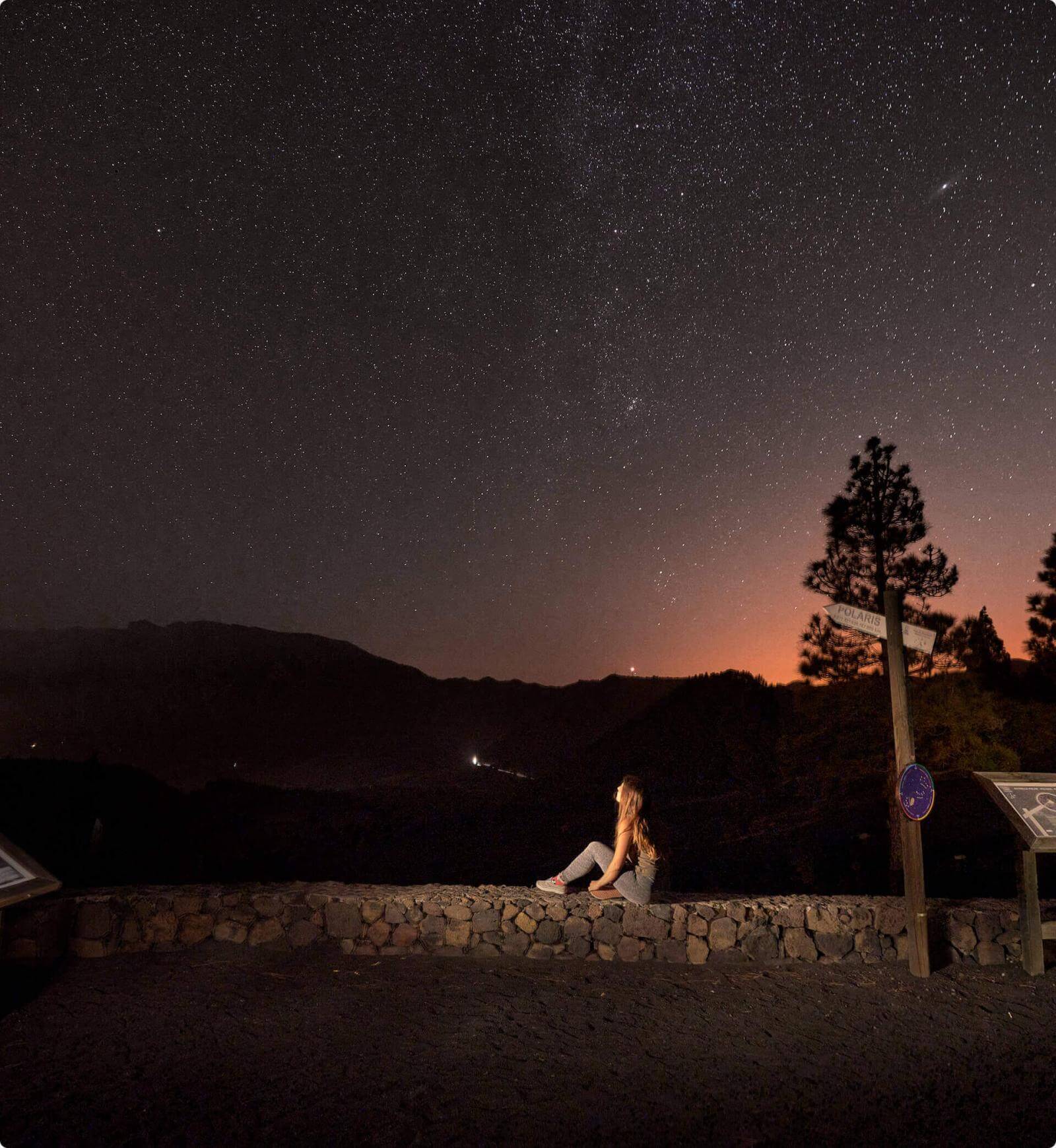 Sterrennacht vanaf het uitzichtpunt Llano del Jable op La Palma, met silhouetten van bergen en een persoon.