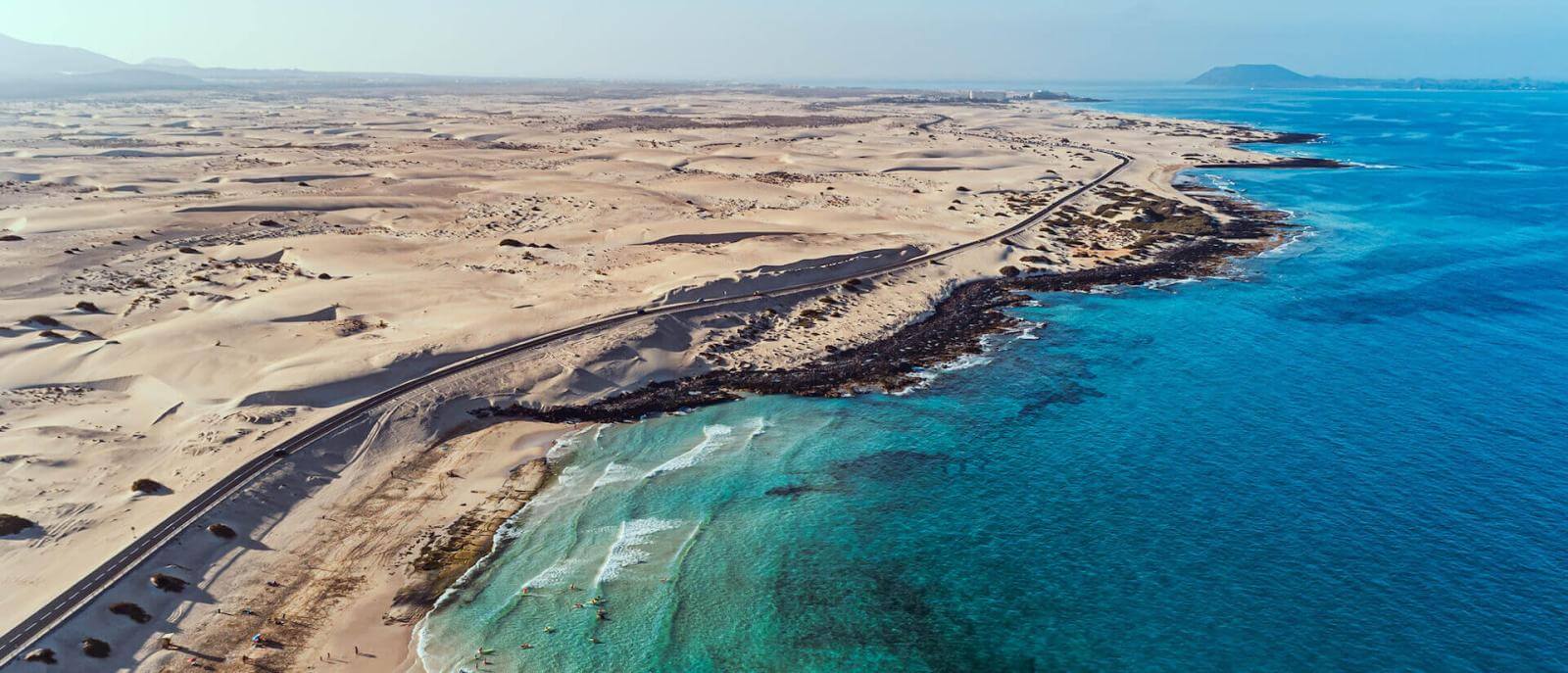 Luchtfoto van de Duinen van Corralejo op Fuerteventura, met zandvlakten naast de turquoise zee.