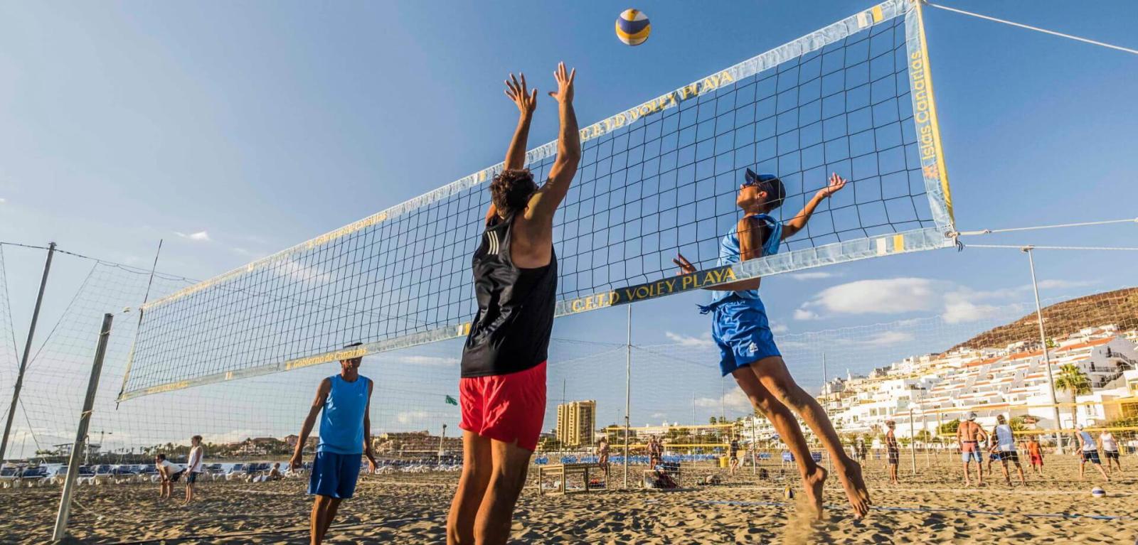 Volleyballers tijdens een beachvolleybadwedstrijd springen om een bal te veroveren.