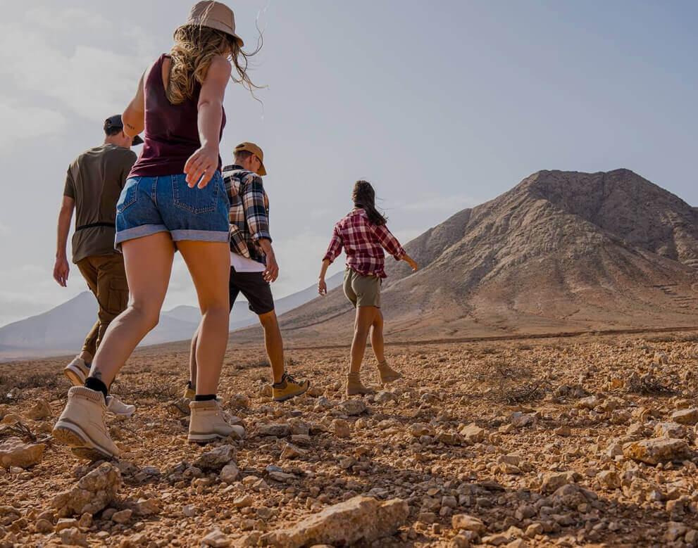 Een groep wandelt door een dor terrein naar een berg in een uitgestrekte natuur.