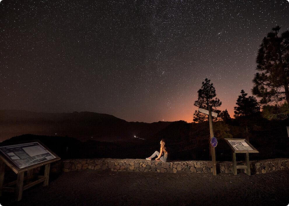 Sterrennacht vanaf het uitzichtpunt Llano del Jable op La Palma, met silhouetten van bergen en een persoon.