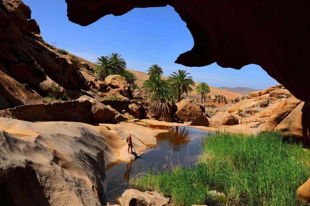 Afgrond van Las Peñitas op Fuerteventura met rotsen, palmbomen en een rivierbedding in een dor landschap.