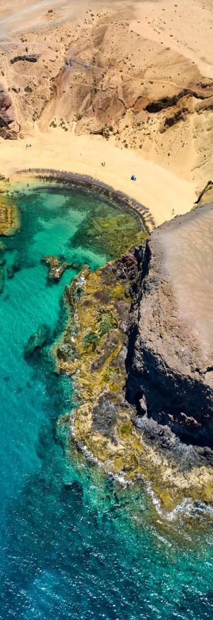 Luchtfoto van het strand van Papagayo op Lanzarote, met goud zand, kliffen en turquoise zee.
